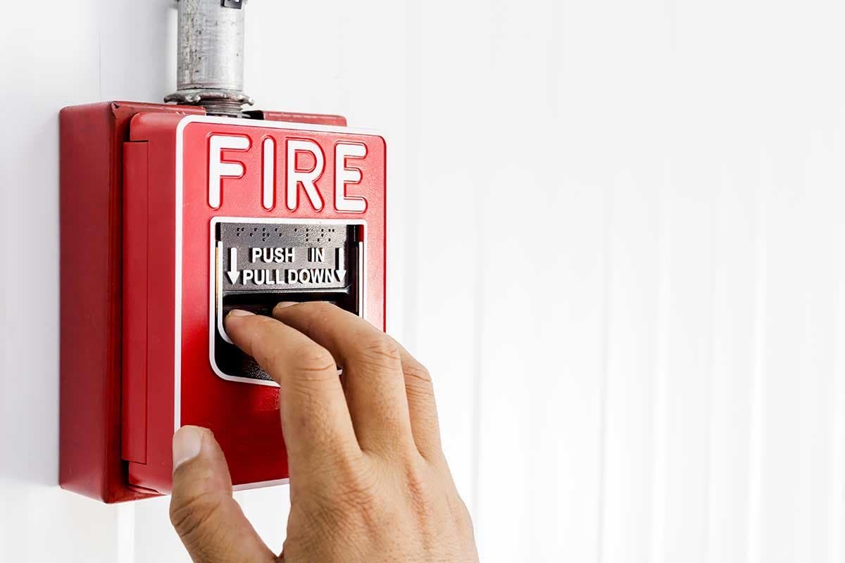 Hand pulling a red fire alarm pull station — serving Marshall, TX